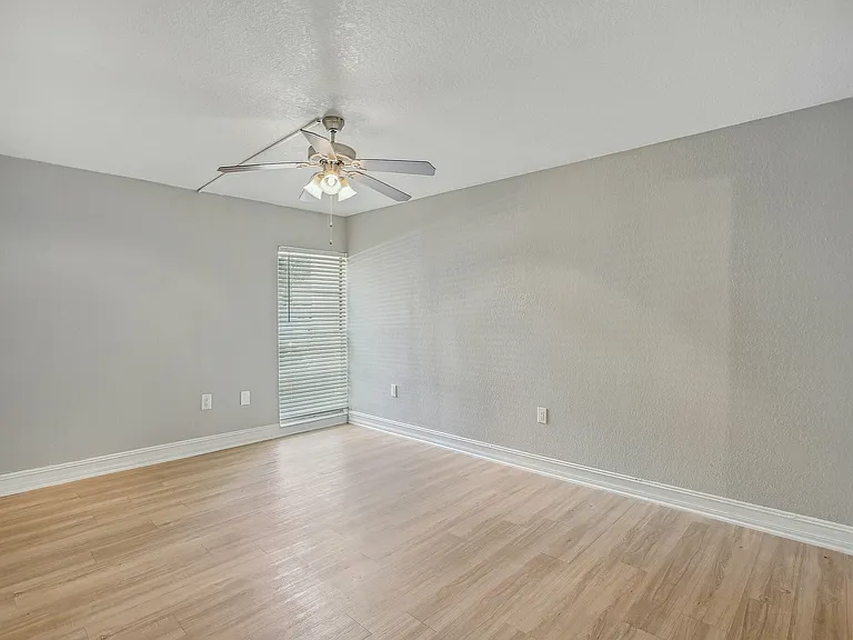 Bright and spacious room with elegant wood flooring, soft gray walls, and a modern ceiling fan, perfect for a cozy living area.