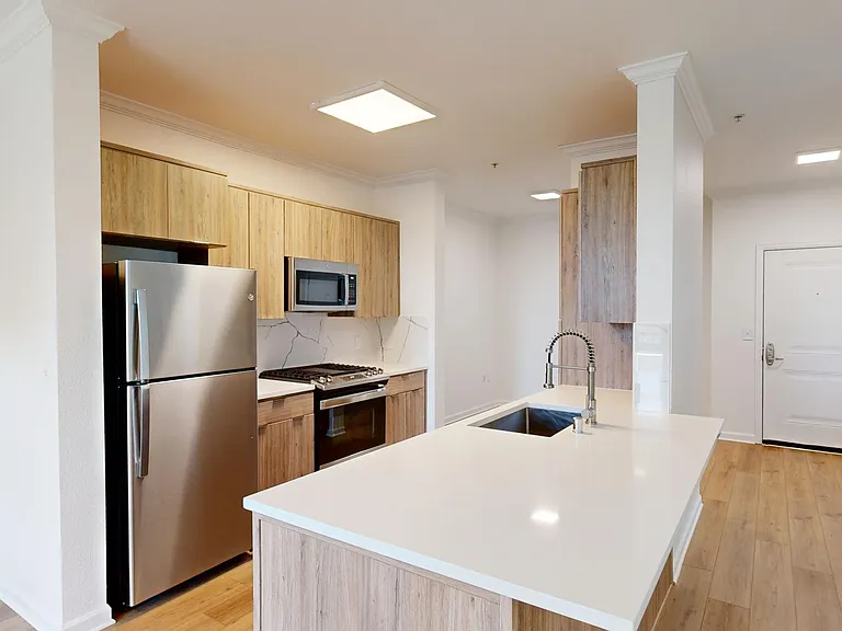 Apartment kitchen with stainless steel appliances, light counters, and wood style floor.