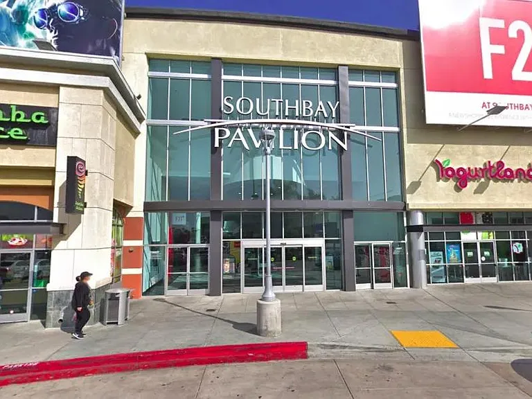 Street-facing retail plaza entrance with glass storefronts and wide sidewalk access near shops and services.