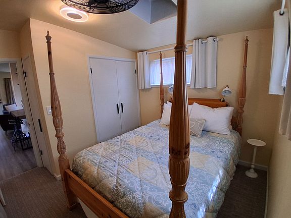 Cozy bedroom with four poster bed. There are black out curtains and a ceiling fan.