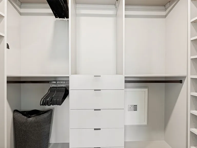 The walk-in closet space has been optimized by California Closets. The object to the lower right is a wall safe.