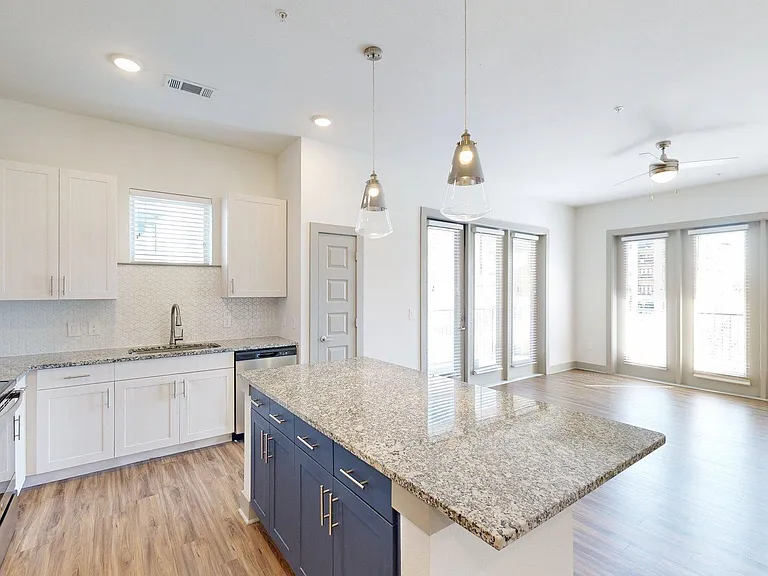 Apartment Kitchen with Stainless Steel Appliances, Dining and Living Room with Wood Style Flooring.