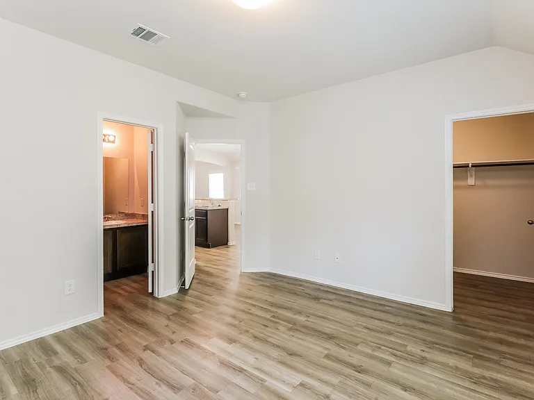 Bright empty room featuring elegant hardwood floors, an open walk-in closet, and doorway leading to a modern bathroom with sleek countertops. Bright empty room featuring elegant hardwood floors, an open walk-in closet, and doorway leading to a modern bath