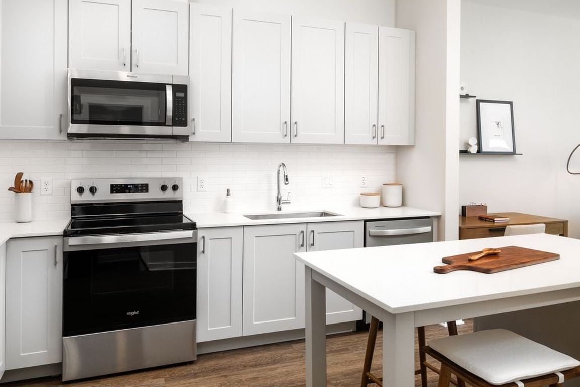 New West Phase - Finish Package III Kitchen with stainless steel appliances, white quartz countertops, grey cabinetry, pendant lighting, and hard surface flooring