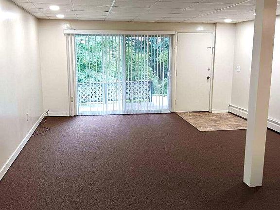 View of living room from the kitchen, showing the front deck and greenery outside.