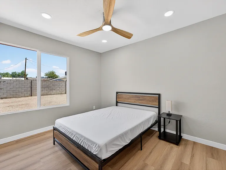 Bedroom features wood-look flooring, a ceiling fan, and a large window for natural light, plus space for a nightstand.