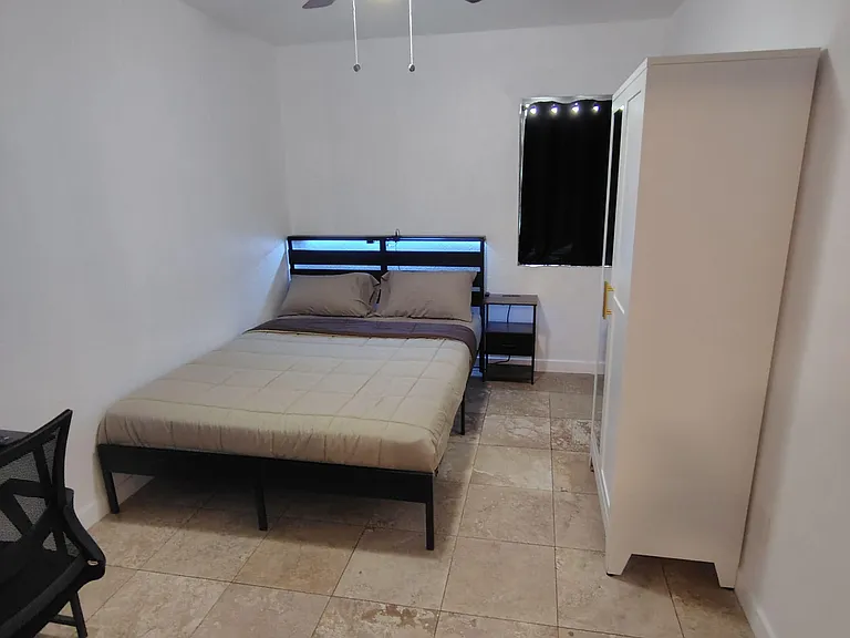 Furnished bedroom with tile flooring, ceiling fan, bedside table, and wardrobe for convenient in-room storage.