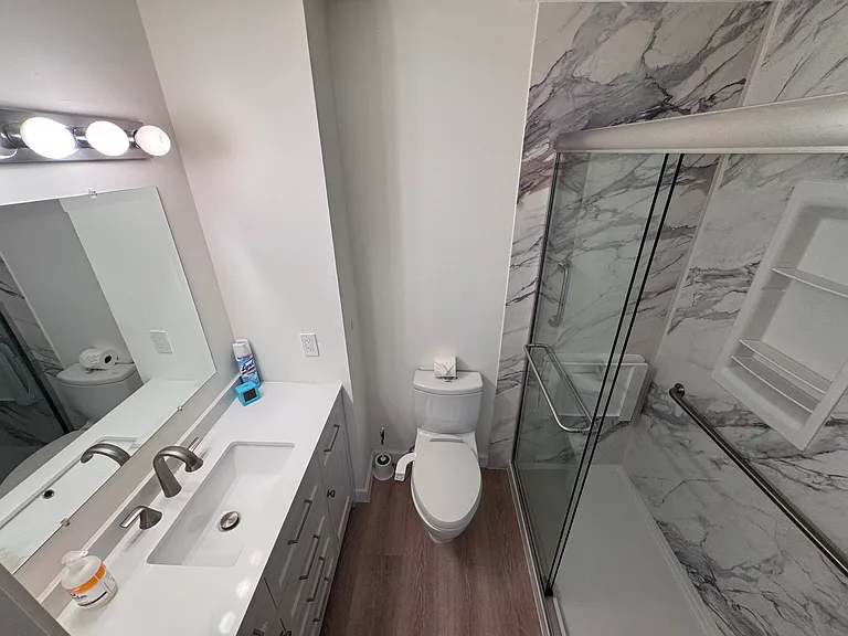 Bathroom adjacent to Bedroom 2. New vanity and toilet with bidet attachment. This bathroom features a walk-in safety shower with slip-resistant flooring, a shower niche with integrated storage, and built-in seating.