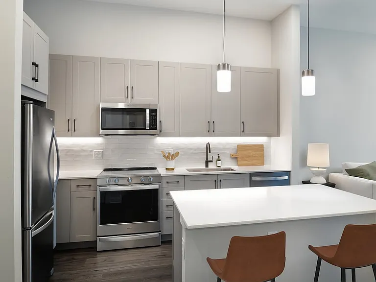 Upgrade Collection II kitchen with stainless steel appliances, grey cabinetry, white quartz countertops, tile backsplash, under-cabinet lighting, and hard surface flooring