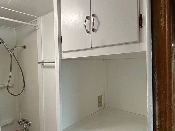 Bathroom tub with overhead shower.
Cabinets and storage shelves.