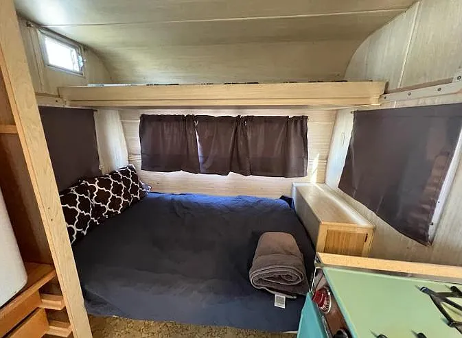 Compact sleeping nook with a full-size bed, built-in shelving, and multiple windows with curtains for added privacy.