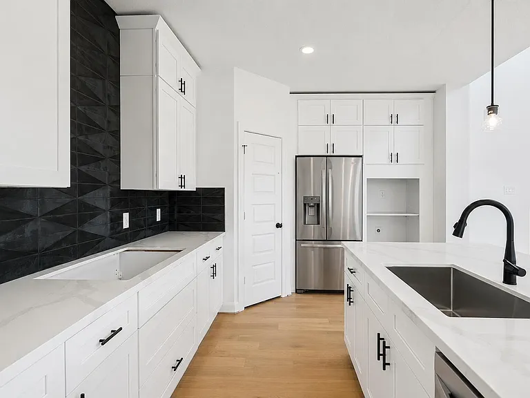 Spacious kitchen with ample white cabinetry, quartz-style counters, a large island sink, and stainless steel refrigerator.