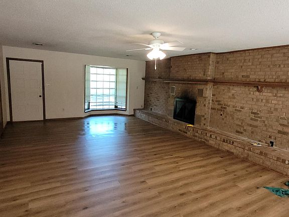 Looking from the Den / Great Room to the Front Door and Bay Window. The brick wall has a ledge and there is a wood burning fireplace.