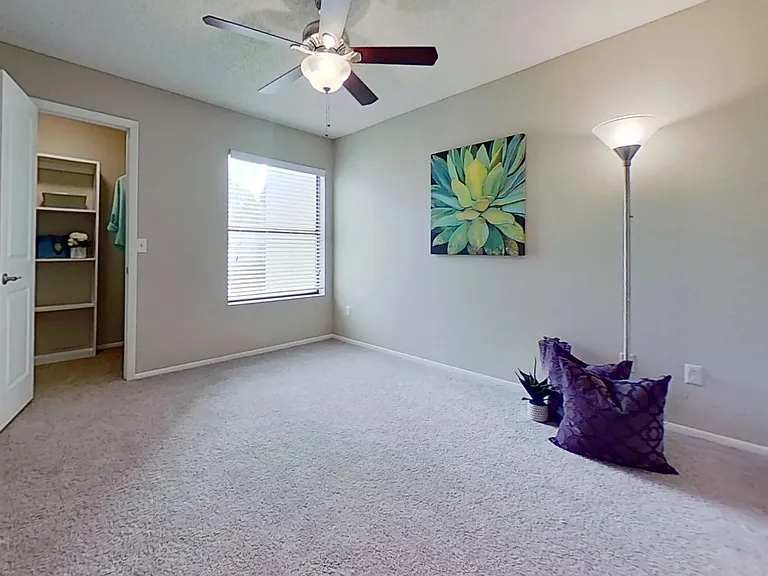 The Martinique Autograph floor plan offers a large bedroom with plush carpeting, a ceiling fan, and direct access to a walk-in closet.