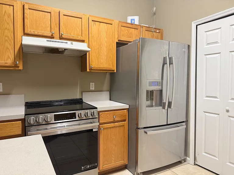 Functional kitchen setup with ample wood cabinetry, laminate counters, and stainless steel appliances including a French-door