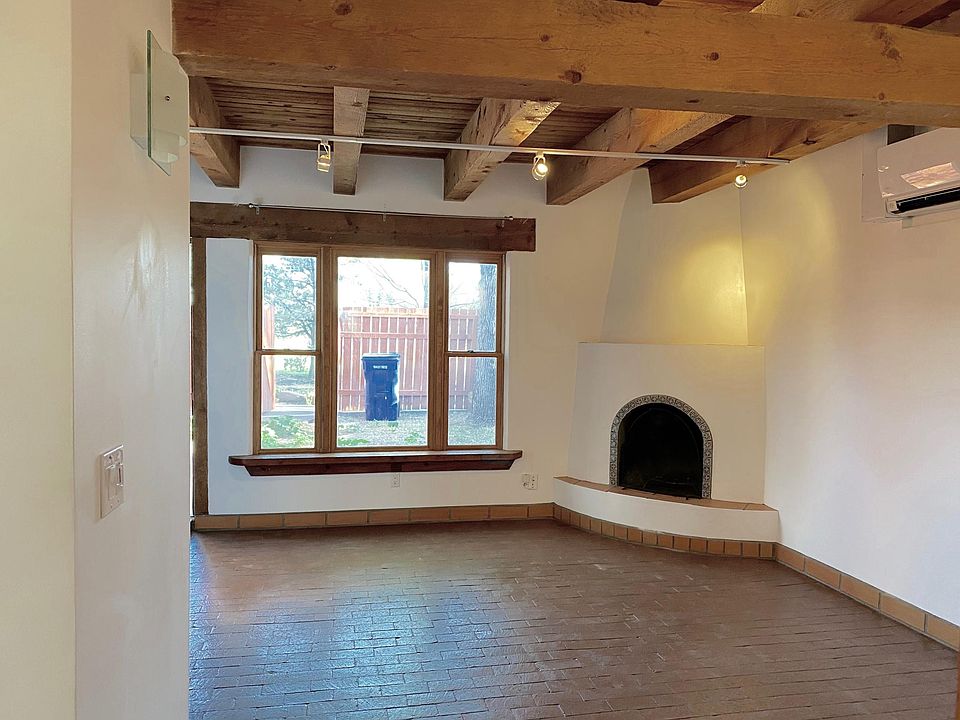 Living room looking out to private, fenced front yard. Brick floors. Beamed ceilings throughout.