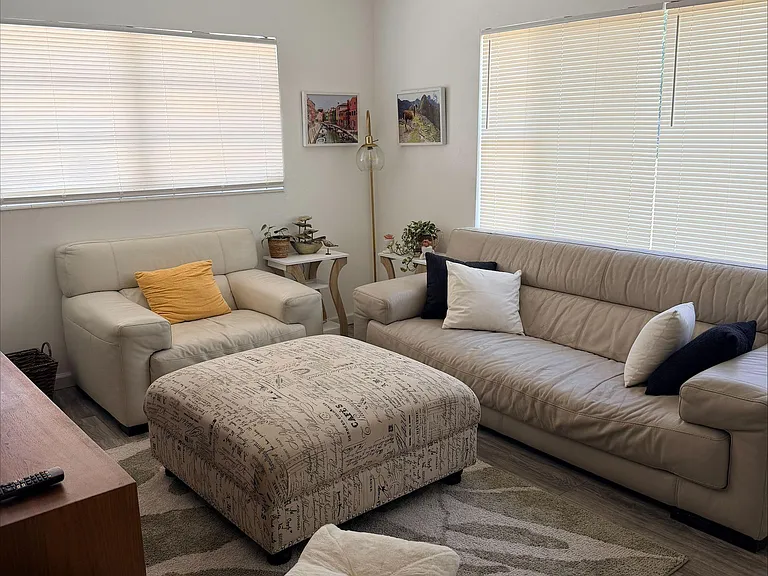 Comfortable living room with two sofas, a large ottoman, ceiling fan, and wide windows with blinds for privacy.