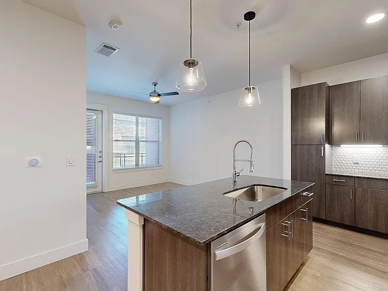 Apartment kitchen with stainless steel appliances and living room with wood-style flooring.