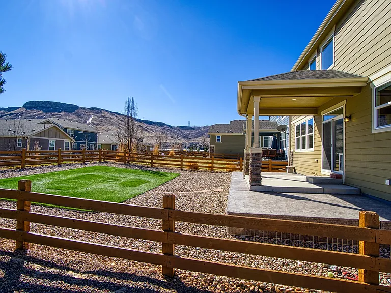No-maintenance fenced-in backyard with realistic artificial grass, river rock, covered patio, natural gas line for grill, and views of North Table Mountain.