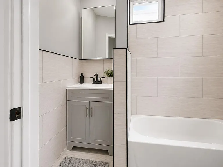 Updated bath with a sleek vanity, large mirror, and tiled tub surround plus a window for natural light.