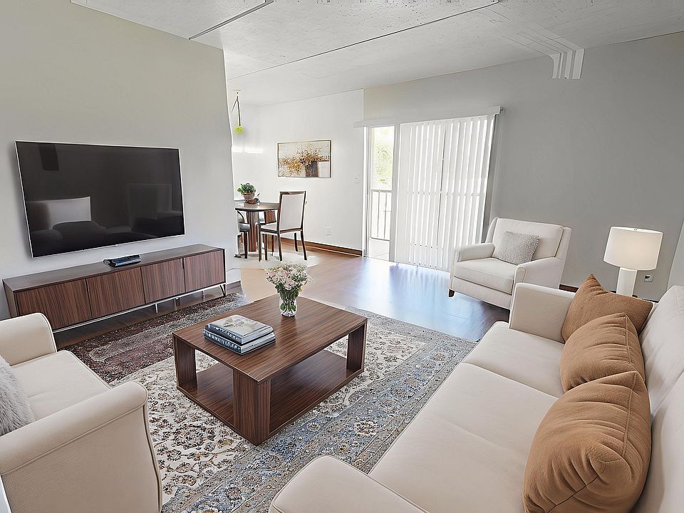 Elegant living room showcasing modern decor, cozy beige sofas, a sleek TV, wooden furniture, and ample natural light from large windows.
