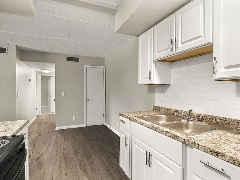 Charming modern kitchen with elegant granite countertops, white cabinetry, and sleek wood flooring leading to a cozy hallway.
