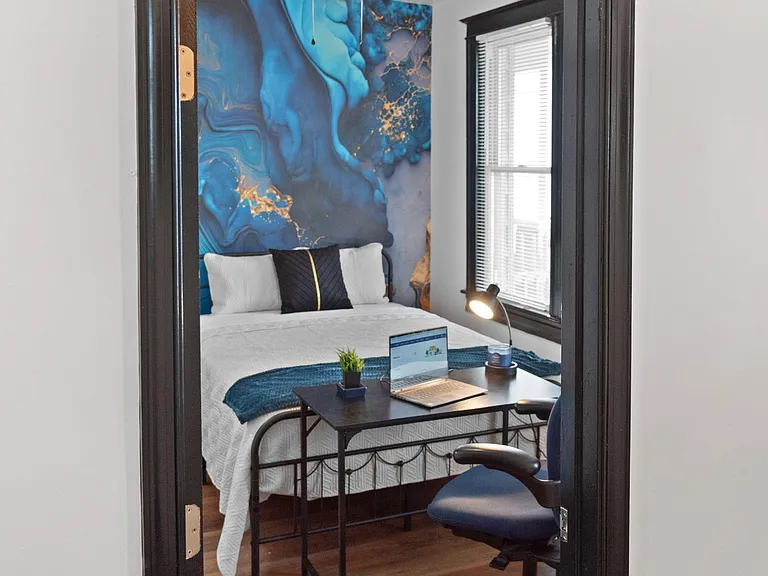 Private bedroom with a queen bed, window with blinds, ceiling fan, and a dedicated desk workspace for study or remote work.