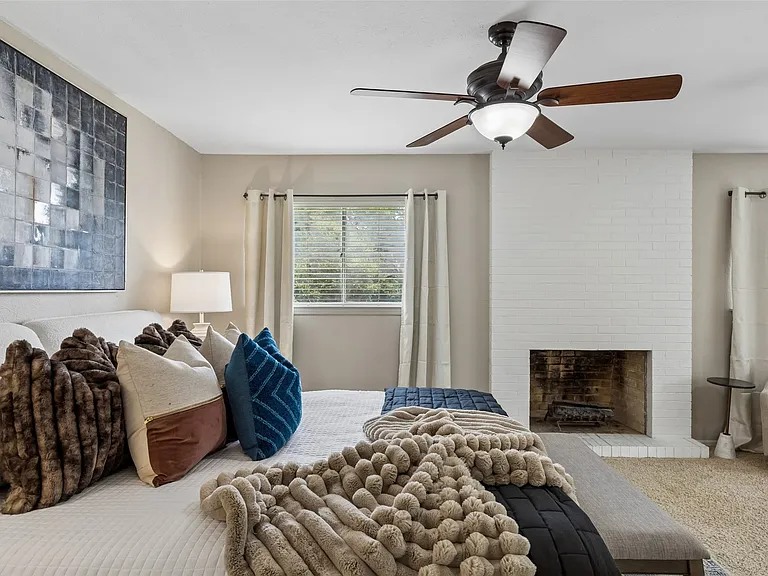 Bedroom featuring a prominent white brick fireplace, multiple windows with blinds, ceiling fans.