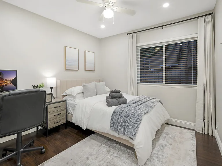 This bedroom includes a comfortable full-size bed with blackout curtains for complete darkness. It has a desk with a laptop monitor and an office chair for a productive workspace. A spacious closet with hangers provides ample storage for clothes.