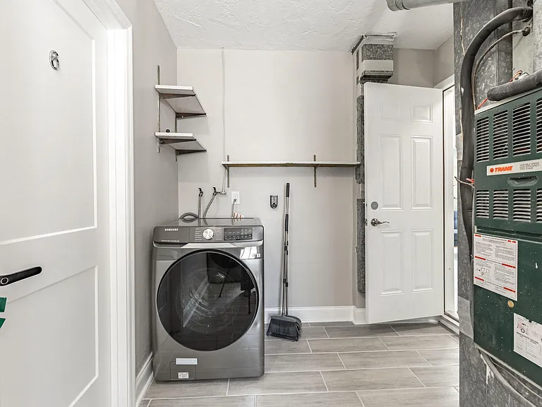 Dedicated laundry/utility room with front-load washer, open shelving, and durable tile flooring for easy upkeep.