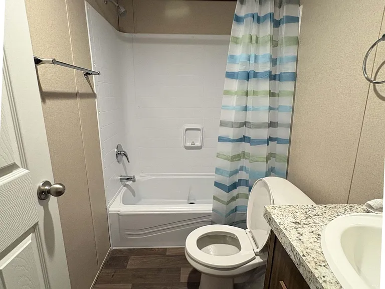 Full bathroom with tub/shower combo, privacy curtain, and a vanity with granite-look countertop and storage below.