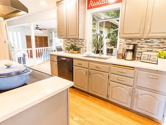 The kitchen area highlighting the tiled back splash, garden window, the Quartz Counters, cooktop, and deep sink.