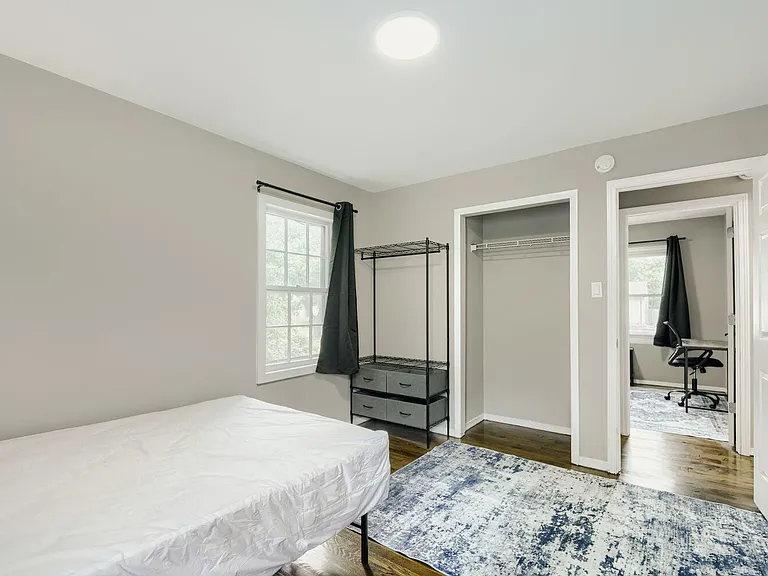 Bedroom offers hardwood floors, a sunlit window, open closet, and space for a bed and storage or a small desk setup.