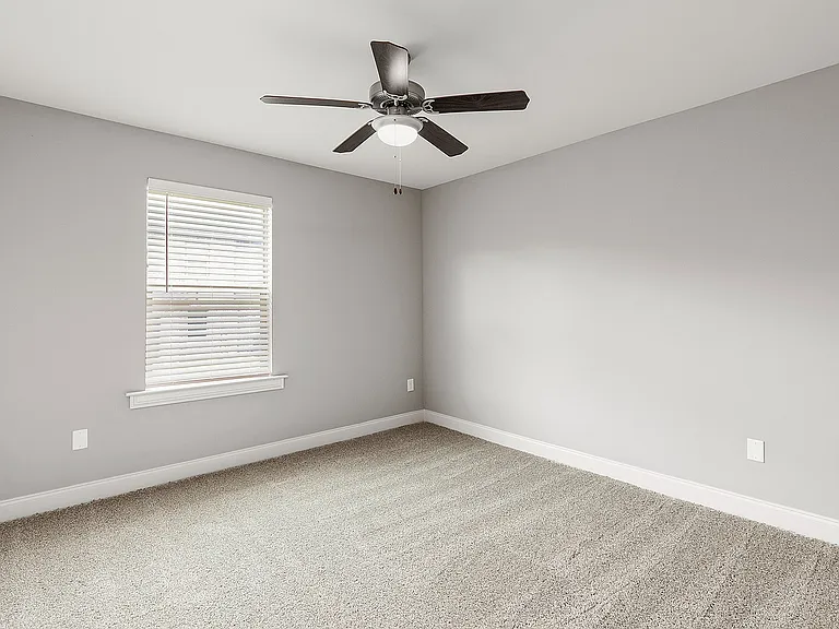 Bright, spacious room with plush carpet, sleek ceiling fan, and elegant window blinds perfect for modern living.