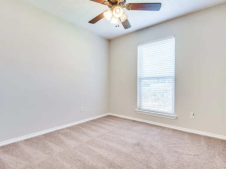 Neutral-toned room featuring a single window with blinds, carpet flooring, a ceiling fan with light fixture, and white trim