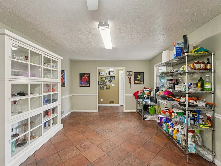 A spacious utility room with warm tile flooring, generous shelving, and charming display cabinetry, offering everyday function with a thoughtfully organized touch.
