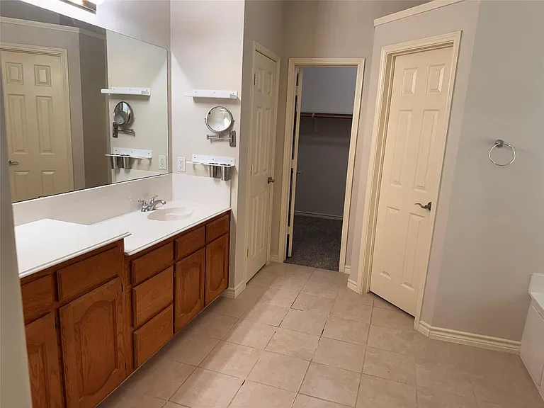 Bathroom featuring a long vanity with dual sinks, laminate countertops, and wood-finish cabinetry