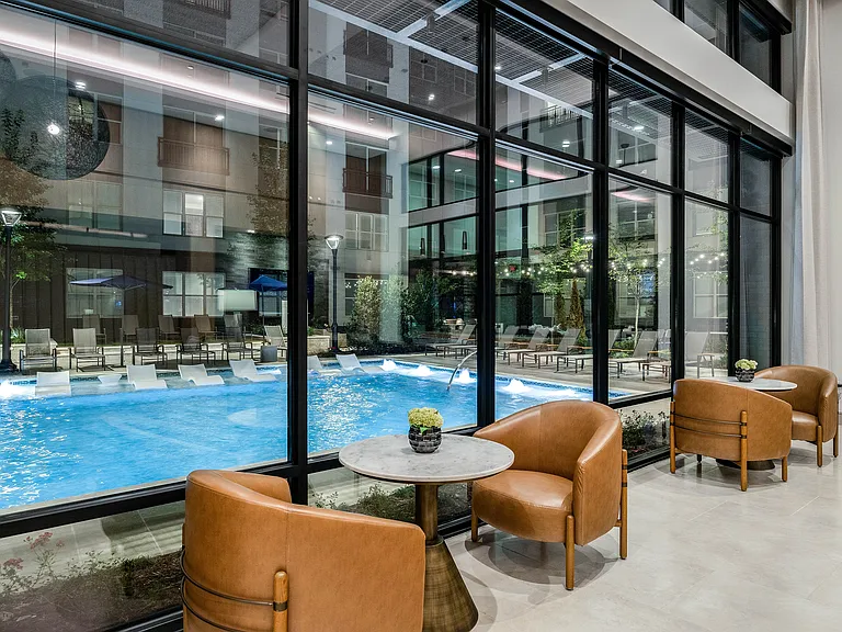 Elegant lounge area with plush leather chairs and a view of a sparkling outdoor pool, surrounded by modern architectural details.