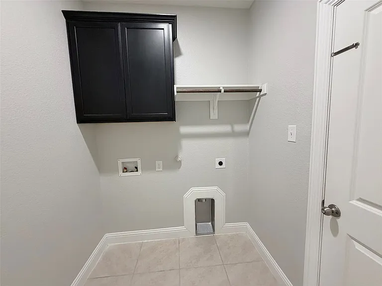 Dedicated laundry room featuring tile flooring, upper cabinetry storage, wall-mounted drying rack, and a pet door for convenient access