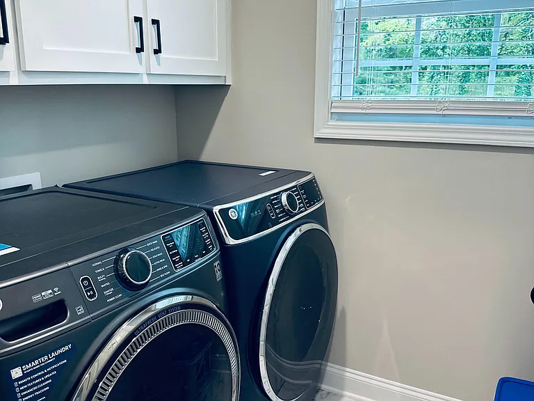 Dedicated laundry area with front-loading washer and dryer, overhead cabinetry, and a window for ventilation.