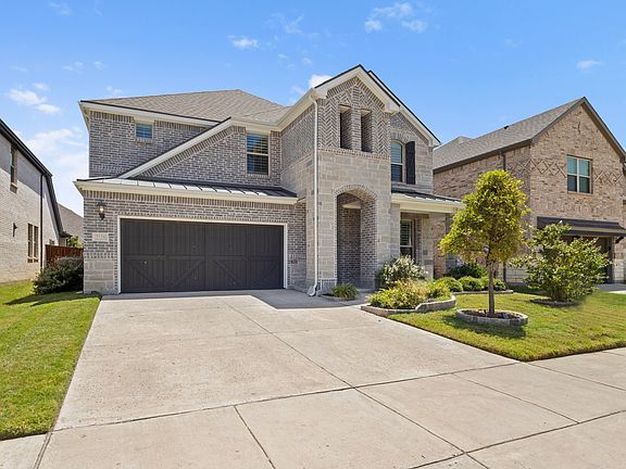 Front of the home with brick and stone siding, 2-car garage, driveway and a front lawn
