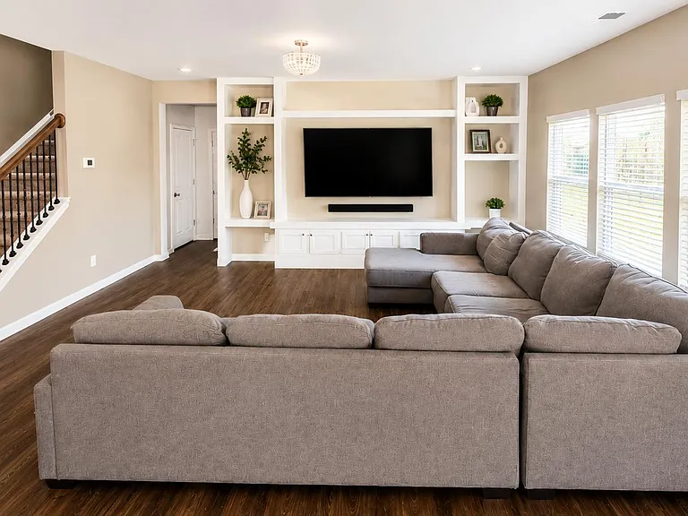 Open living room with built-in media wall, ample seating area, and large windows with blinds for natural light.