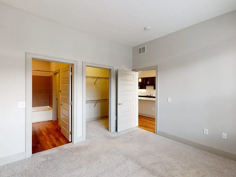Spacious apartment bedroom with large closet, attached bathroom and plush carpet flooring.