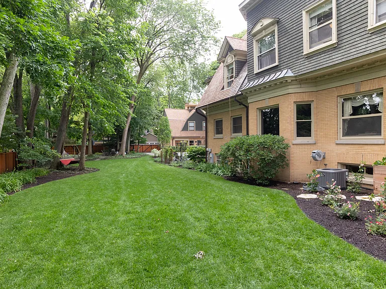 Landscaped lawn with garden beds surrounding with various trees lining the edge of property