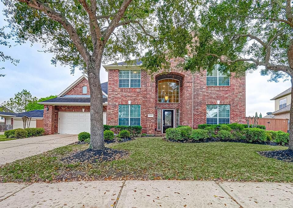 Stunning 2-story home with an immaculate front yard has pretty green shrubs and mature trees.