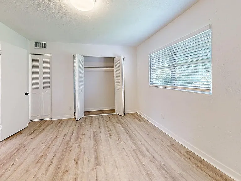 Bright, airy room with elegant hardwood floors and a spacious closet, illuminated by abundant natural light through large windows.