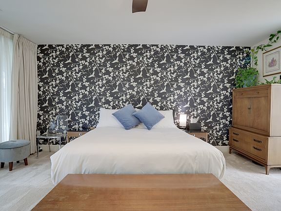 The spacious primary bedroom is in the back of the house and overlooks the patio and cherry tree. Features a queen-sized bed, dresser, privacy and blackout curtains, large closet, and ensuite bathroom.