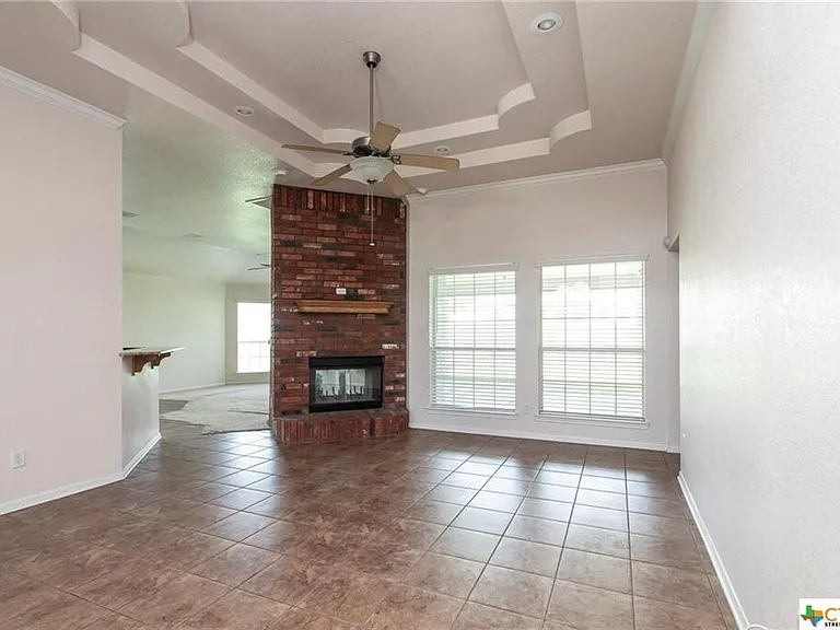 Picture frame ceiling in living room with ceiling fan. Pass through brick fireplace to family room.