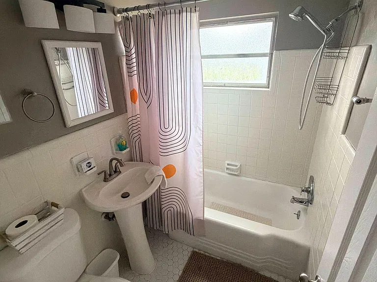 Full bath with tub/shower combo, tiled surround, privacy window, and vanity storage for everyday essentials.