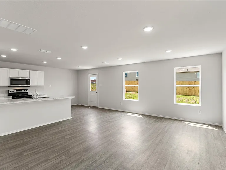 Open-concept living area featuring wood-finish flooring, recessed lighting, and a kitchen with white cabinetry and a stainless steel appliance suite
